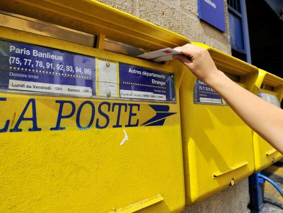 Une personne met une enveloppe dans une des 2 boites aux lettres de la Poste
