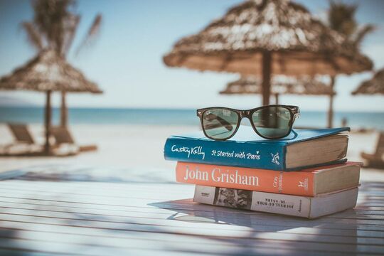 Des livres se trouvent sur le sable et sous le parasol