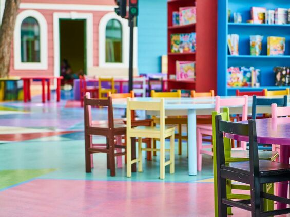 Des petites chaises d'école de toutes les couleurs mises autour de petites tables dans une salle de classe