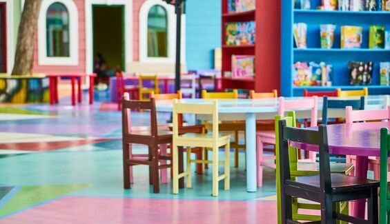 Des petites chaises d'école de toutes les couleurs mises autour de petites tables dans une salle de classe